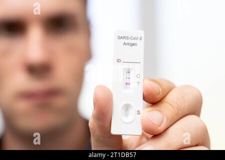 Augsburg, Bayern, Deutschland. Oktober 2023. Der Mann zeigt positiven COVID-19-Coronavirus-Schnelltest. Testkassette mit zwei Schlägen, Ergebnis positive FOTOMONTAGE *** Mann zeigt einen positiven COVID-19 Coronavirus Schnelltest. Testkasette mit zwei Strichen, Ergebnis positiv FOTOMONTAGE Credit: Imago/Alamy Live News Stockfoto