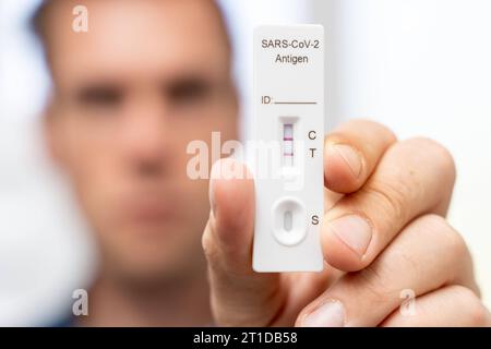 Augsburg, Bayern, Deutschland. Oktober 2023. Der Mann zeigt positiven COVID-19-Coronavirus-Schnelltest. Testkassette mit zwei Schlägen, Ergebnis positive FOTOMONTAGE *** Mann zeigt einen positiven COVID-19 Coronavirus Schnelltest. Testkasette mit zwei Strichen, Ergebnis positiv FOTOMONTAGE Credit: Imago/Alamy Live News Stockfoto