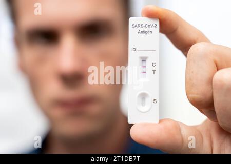 Augsburg, Bayern, Deutschland. Oktober 2023. Der Mann zeigt positiven COVID-19-Coronavirus-Schnelltest. Testkassette mit zwei Schlägen, Ergebnis positive FOTOMONTAGE *** Mann zeigt einen positiven COVID-19 Coronavirus Schnelltest. Testkasette mit zwei Strichen, Ergebnis positiv FOTOMONTAGE Credit: Imago/Alamy Live News Stockfoto