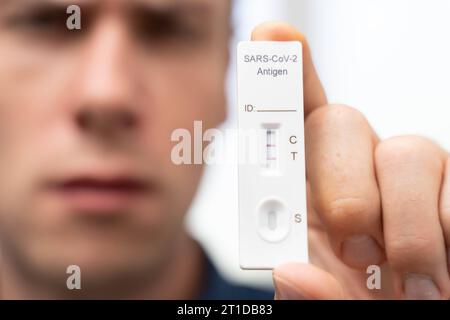 Augsburg, Bayern, Deutschland. Oktober 2023. Der Mann zeigt positiven COVID-19-Coronavirus-Schnelltest. Testkassette mit zwei Schlägen, Ergebnis positive FOTOMONTAGE *** Mann zeigt einen positiven COVID-19 Coronavirus Schnelltest. Testkasette mit zwei Strichen, Ergebnis positiv FOTOMONTAGE Credit: Imago/Alamy Live News Stockfoto