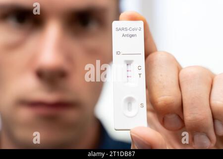 Augsburg, Bayern, Deutschland. Oktober 2023. Der Mann zeigt positiven COVID-19-Coronavirus-Schnelltest. Testkassette mit zwei Schlägen, Ergebnis positive FOTOMONTAGE *** Mann zeigt einen positiven COVID-19 Coronavirus Schnelltest. Testkasette mit zwei Strichen, Ergebnis positiv FOTOMONTAGE Credit: Imago/Alamy Live News Stockfoto