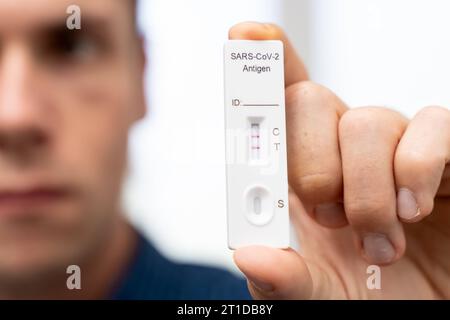 Augsburg, Bayern, Deutschland. Oktober 2023. Der Mann zeigt positiven COVID-19-Coronavirus-Schnelltest. Testkassette mit zwei Schlägen, Ergebnis positive FOTOMONTAGE *** Mann zeigt einen positiven COVID-19 Coronavirus Schnelltest. Testkasette mit zwei Strichen, Ergebnis positiv FOTOMONTAGE Credit: Imago/Alamy Live News Stockfoto