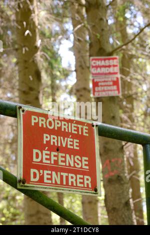 „Privateigentum. Kein Betreten“ Schild auf einem Zaun am Eingang zu einem privaten Wald. Im Hintergrund steht das Schild „Privat, No Wilderer“ auf einem Baum Stockfoto