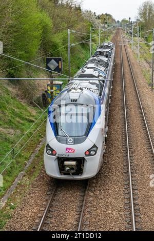 Durchfahrt des TER-Lokalzuges auf der Eisenbahnverbindung zwischen Paris, Rouen und Le Havre in der Normandie. Eisenbahnstrecke und Oberleitung Stockfoto