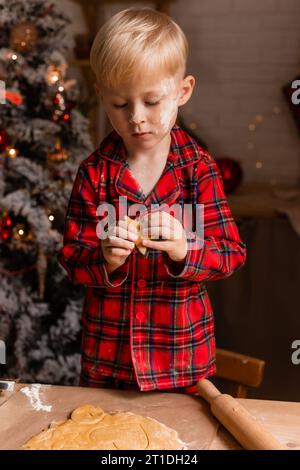 Der Junge im roten karierten Pyjama kocht Weihnachtskekse in der Küche. Kleiner Koch. Hochwertige Fotos Stockfoto