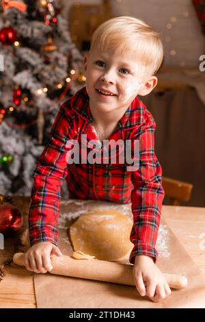 Der Junge im roten karierten Pyjama kocht Weihnachtskekse in der Küche. Kleiner Koch. Hochwertige Fotos Stockfoto