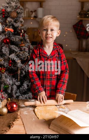 Der Junge im roten karierten Pyjama kocht Weihnachtskekse in der Küche. Kleiner Koch. Hochwertige Fotos Stockfoto