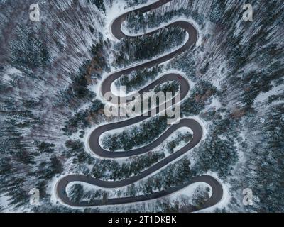 Von oben nach unten auf die winterliche kurvenreiche Straße im dichten Wald, Transsilvanien, Rumänien. Stockfoto