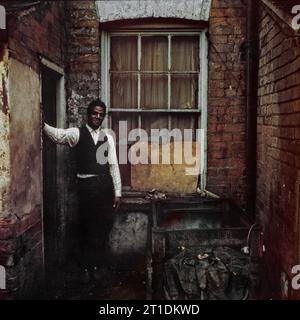 Der schwarze Mann stand während der Räumung und des Abbruchs des Slums in St. Ann's, Nottingham, England, in der Eingangstür seines viktorianischen Reihenhauses. 1969-1972 Stockfoto