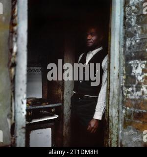 Der schwarze Mann stand während der Räumung und des Abbruchs des Slums in St. Ann's, Nottingham, England, in der Eingangstür seines viktorianischen Reihenhauses. 1969-1972 Stockfoto