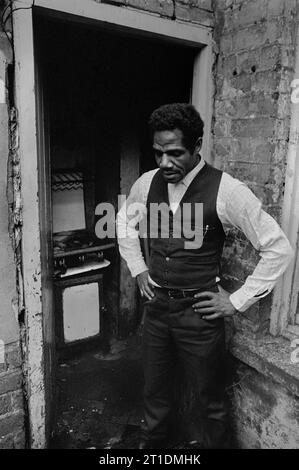 Der schwarze Mann stand während der Räumung und des Abbruchs des Slums in St. Ann's, Nottingham, England, in der Eingangstür seines viktorianischen Reihenhauses. 1969-1972 Stockfoto