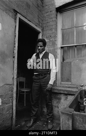 Der schwarze Mann stand während der Räumung und des Abbruchs des Slums in St. Ann's, Nottingham, England, in der Eingangstür seines viktorianischen Reihenhauses. 1969-1972 Stockfoto