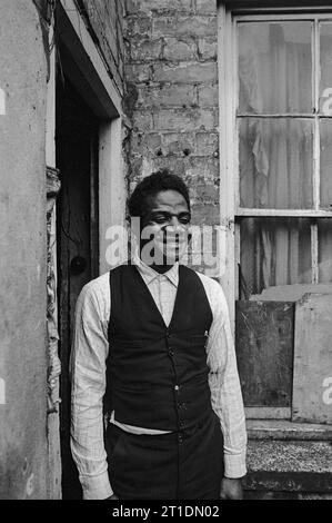 Der schwarze Mann stand während der Räumung und des Abbruchs des Slums in St. Ann's, Nottingham, England, in der Eingangstür seines viktorianischen Reihenhauses. 1969-1972 Stockfoto