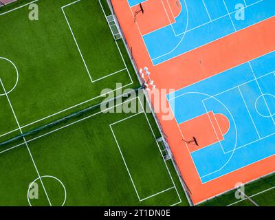 Aus der Vogelperspektive auf ein grünes Fußballfeld und einen farbenfrohen Basketballplatz, der einen Blick auf zwei verschiedene Sporteinrichtungen nebeneinander bietet. Das Gegenteil Stockfoto