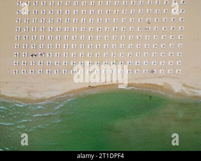 Am Meer erstreckt sich ein Sandstrand, der mit leeren Liegestühlen geschmückt ist. Aus der Luftperspektive entfaltet sich die ruhige Szene mit dem azurblauen Meer Stockfoto