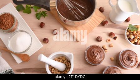 Tisch voller Zutaten, die in Schüsseln zubereitet werden, um hausgemachte Haselnusscreme zu machen. Draufsicht. Stockfoto