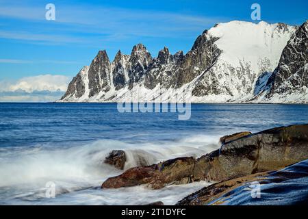 Surfen Sie an der felsigen Küste von Tungeneset mit Teufelszähnen im Hintergrund, Ersfjord, Okshornan, Tungeneset, Senja, Troms og Finnmark, Norwegen Stockfoto