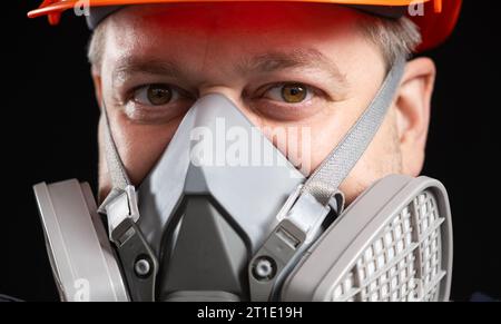 Ein Mann mit Schutzhelm und Atemschutzmaske zum Schutz vor Staub und Gasen auf schwarzem Hintergrund. Stockfoto