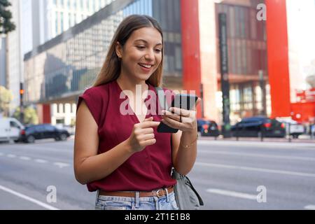 Brasilianische junge Geschäftsfrau nutzt Handy-App für Internet-Banking auf der Paulista Avenue, Sao Paulo, Brasilien Stockfoto