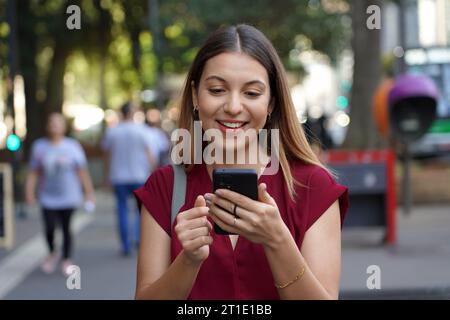 Nahaufnahme einer jungen, stilvollen Frau, die ein Smartphone mit Ringhalter benutzt, um Diebstähle auf der Straße in der Metropole mit verschwommenen Menschen im Hintergrund zu vermeiden Stockfoto