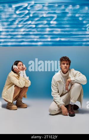 Modisch gekleidetes interrassisches Paar, das sich in der Nähe von blauer Plastikfolie im Studio ausgibt Stockfoto