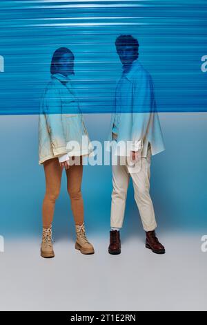 In voller Länge eines interrassischen Paares in Lederstiefeln hinter blauer Plastikfolie im Studio, Wintertrend Stockfoto