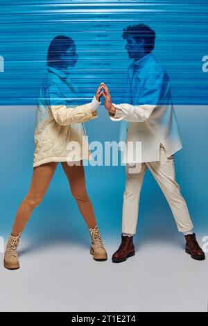 Die ganze Länge eines trendigen, interrassischen Paares, das sich die Hände hinter blauer Plastikfolie berührt Stockfoto