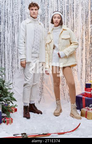 Interracial Models, die in der Nähe des weihnachtsbaums in die Kamera schauen und Geschenke auf silbernem Lametta Hintergrund Stockfoto