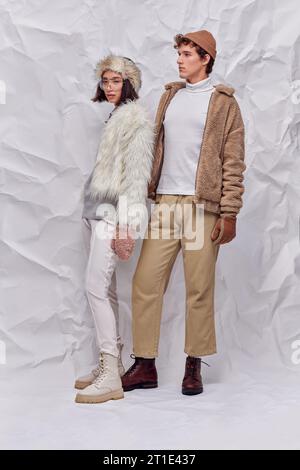 Trendige Interracial-Modelle in Winteroutfits vor weißem strukturiertem Hintergrund, moderner Trend Stockfoto