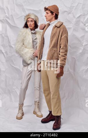 Modisch gekleidetes, interrassisches Paar, das vor weißem Hintergrund wegschaut, stilvoller Winter Stockfoto