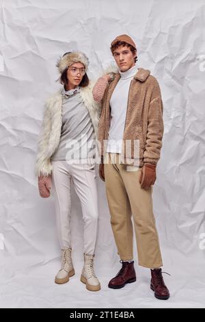 Lange, interrassische Paare in warmer Kleidung auf weißem, strukturiertem Hintergrund, Winterstil Stockfoto
