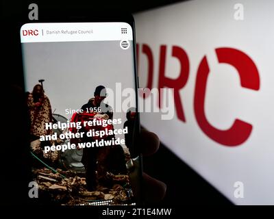 Person mit Handy mit Webseite der humanitären Organisation Danish Refugee Council (DRK) mit Logo. Konzentrieren Sie sich auf die Mitte des Telefondisplays. Stockfoto