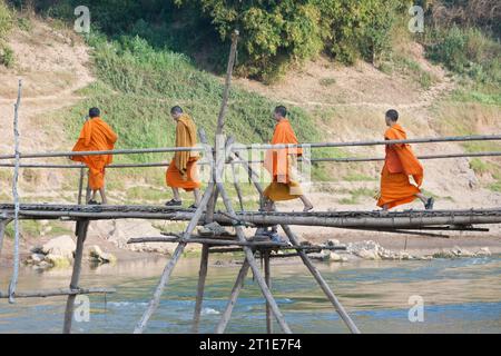 Eine Gruppe junger buddhistischer Mönche, die auf einer Bambusbrücke über den Fluss Nam Khan laufen, Luang Prabang, Laos Stockfoto