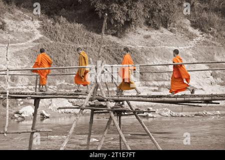 Eine Gruppe junger buddhistischer Mönche, die auf einer Bambusbrücke über den Fluss Nam Khan laufen, Luang Prabang, Laos Stockfoto