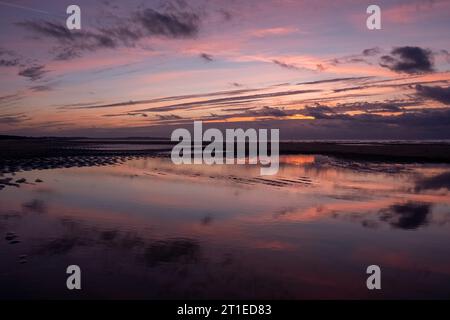 Ein atemberaubender Moment, während die goldene Sonne über einem malerischen französischen Strand untergeht und warme Farbtöne an der Küste ausstrahlt, mit kleinen Wellen, die sanft unter dramatischen Wolken hereinrollen. Goldener Sonnenuntergang am French Beach. Hochwertige Fotos Stockfoto