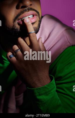 Beschnittene Ansicht eines jungen Mannes mit Zahnspangen und Ringen, der seine Lippe mit dem Finger berührt, Modekonzept Stockfoto