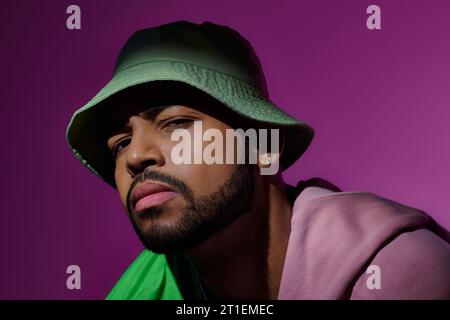 Hübscher junger Mann im grünen panama mit Ohrring, der verdächtig in die Kamera schaut, Modekonzept Stockfoto