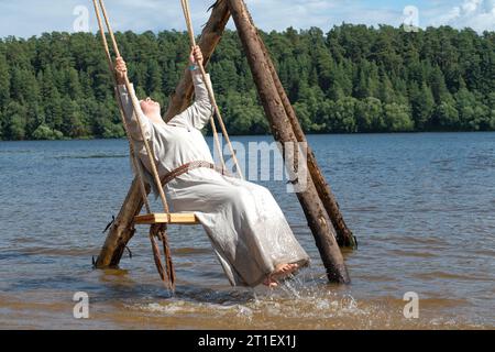 TVER REGION, RUSSLAND - 22. JULI 2023: Ein Mädchen in antikem Kleid, das an einem sonnigen Julitag auf einer Schaukel auf der Wolga schwingt. Historisches Festival „Epic Stockfoto