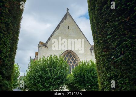 Angers, Frankreich, 2023. Im formellen Garten kann man die Kapelle aus dem 15. Jahrhundert und ihr Buntglasfenster durch den Bogen einer Eibenkippe sehen Stockfoto