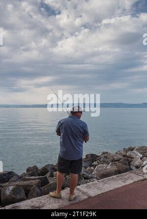 Evian-les-Bains, Frankreich. Ein Fischer am Seeufer, bei Sonnenuntergang. Evian-les-Bains ist eine Stadt im nördlichen Teil des Departements Haute-Savoie (R Stockfoto