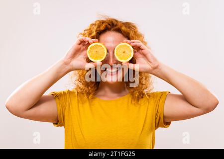 Glückliche Ingwerfrau bedeckt ihre Augen mit Zitronenscheiben. Stockfoto