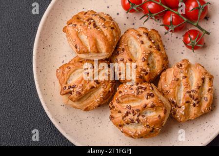 Köstliche knusprige Mini-Puffs mit Wurst oder Fleisch mit Salz, Thymian und Sesam auf dunklem Betonhintergrund Stockfoto