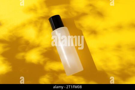 Weiße Flasche Kosmetik, Shampoo, Gel auf gelbem Hintergrund. Platz für Text. Harte Schatten. Kopierbereich. Hintergrund mit tropischem Pflanzenschatten. Stockfoto