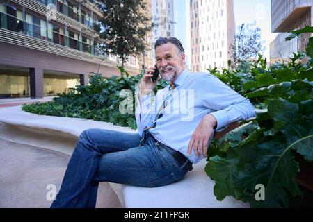 Attraktiver Geschäftsmann, der vor dem Büro sitzt und ein ruhiges Handy spricht. Senior Professional. Stockfoto