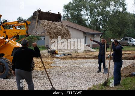 Frontlader entladen von gebrochenem Stein vor Arbeitern mit Schaufeln auf der Baustelle in Tula, Russland Stockfoto