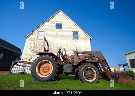 Ein alter rostiger Traktor, der auf dem Rasen eines verwitterten Hauses in North Rustico, Prince Edward Island, Kanada, geparkt wurde Stockfoto