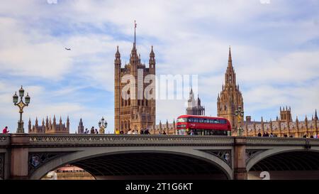 London, England, 6. Oktober 2023: Einige Leute und ein Doppeldeckerbus überqueren die Westminster Bridge. Parlamentsgebäude im Hintergrund. Stockfoto