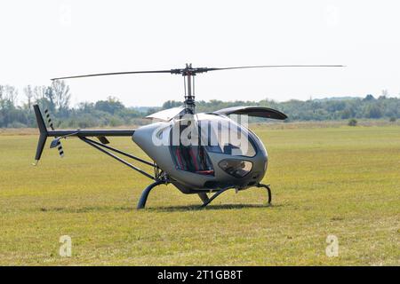 Moderner grauer, kleiner Hubschrauber mit offenen Türen auf einem grasbewachsenen Flugplatz Stockfoto