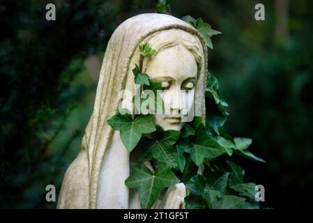 Porträt einer Frauenfigur mit Kopftuch und Efeu-Schal auf einem Friedhof Stockfoto