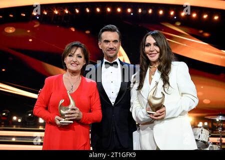 Leipzig, Deutschland. Oktober 2023. Sängerin Ute Freudenberg (l) und Schauspielerin Simone Thomalla (r) stehen mit ihren Trophäen neben Moderator Florian Silbereisen nach der Preisverleihung „Goldene Henne“ auf der Bühne. Der Publikumspreis wird zum 29. Mal auf einer TV-Gala in Leipzig verliehen. Quelle: Hendrik Schmidt/dpa/Alamy Live News Stockfoto